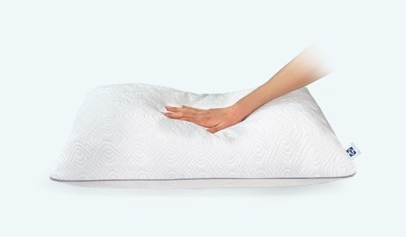 A Sealy Adjustable pillow laying flat, with a hand pushing down on the center, to demonstrate the pillow's plushness