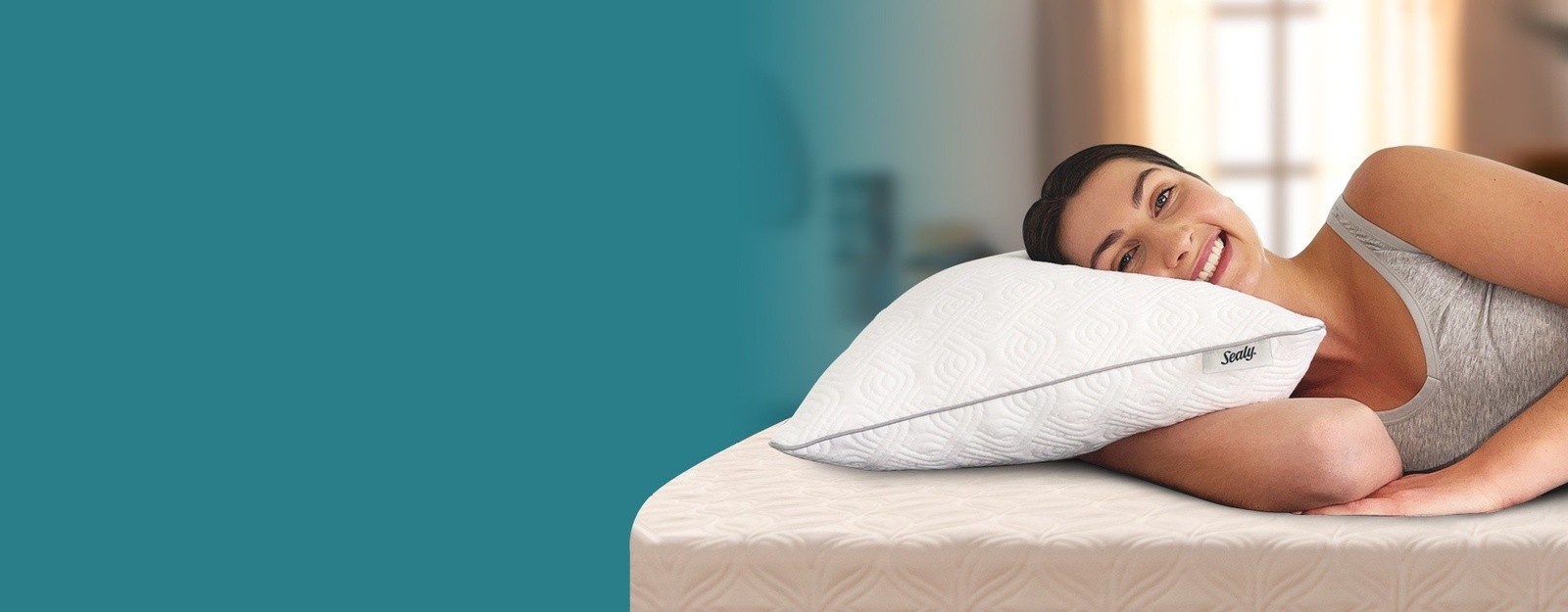 A woman laying on the bed, facing the camera and smiling, as she rests her head on a Sealy Adjustable Pillow